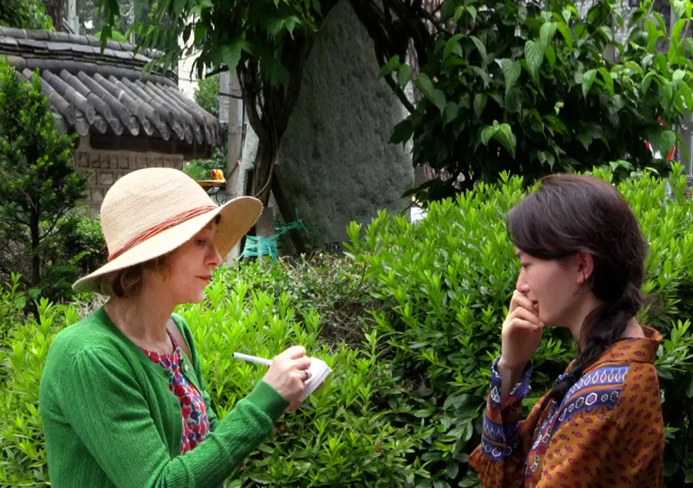 Two women stand facing each other in a garden