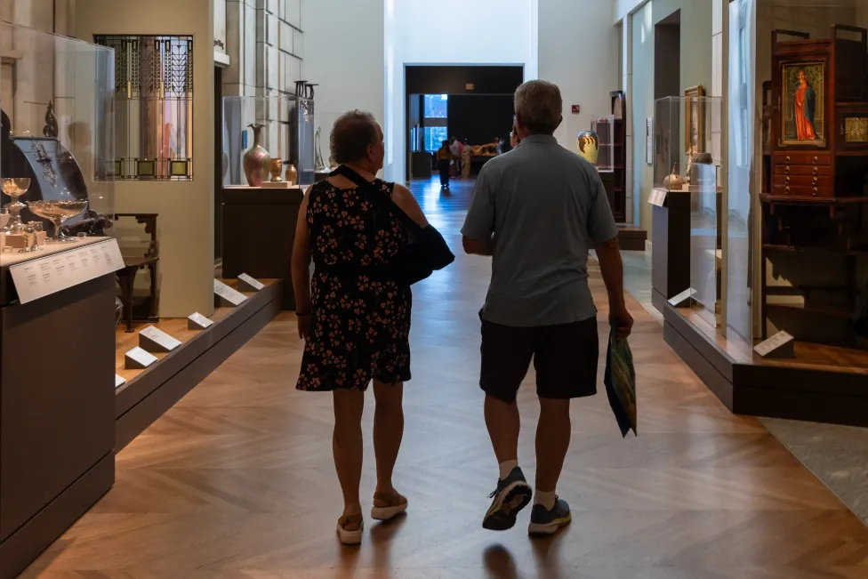 Two people walking down a hallway filled with artworks in the Detroit Institute of Arts.