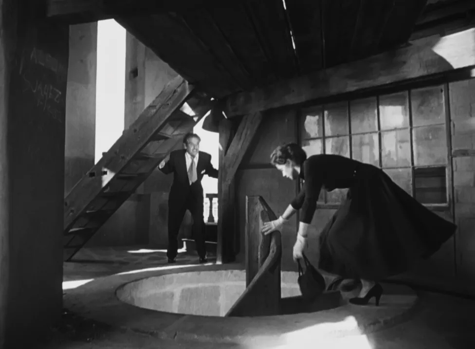 A woman starting down a spiral staircase with a man chasing behind