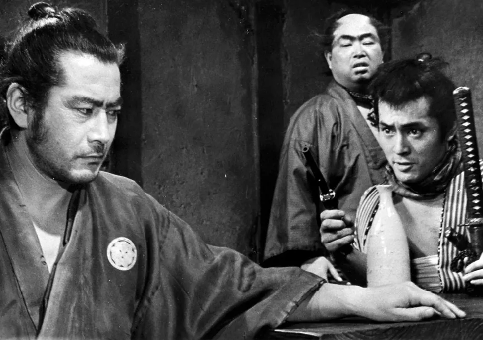 A man being threatened with a weapon by two others