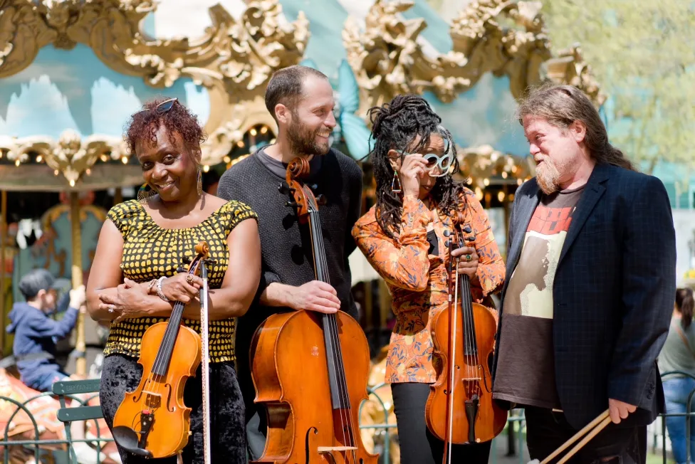 Four musicians holding their instruments, standing together