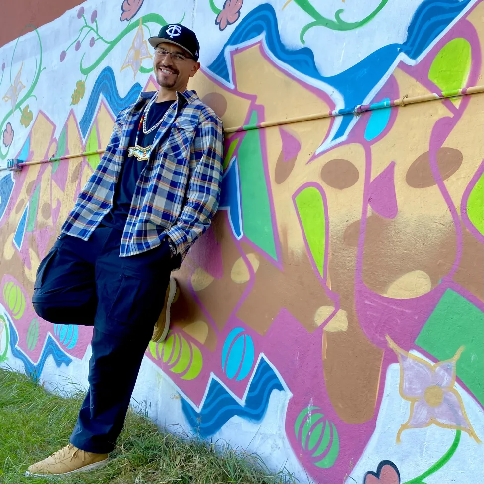 Thomas X stands against a colorful mural