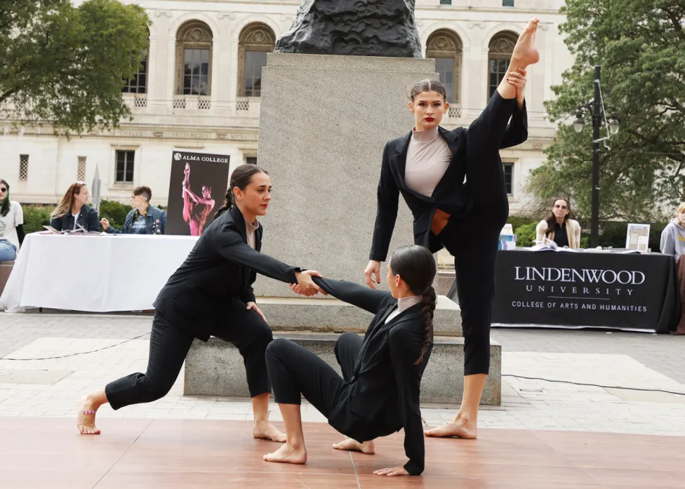 Three dancers performing in front of a large statue