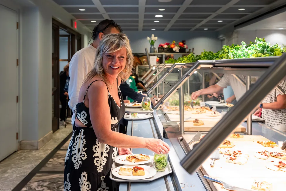 A smiling woman getting her plate at a salad bar