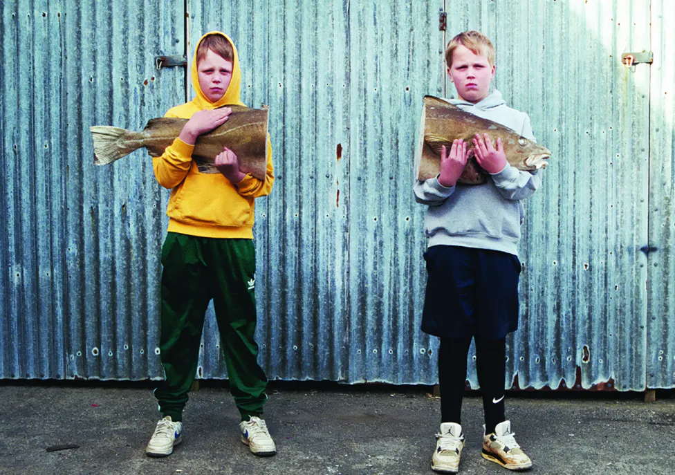 Two young boys holding one half of a large fish