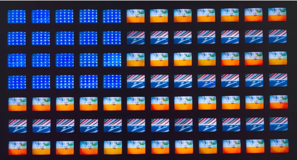 Image of Video Flag XGrid of small video screens arranged like a flag, displaying shifting patterns of blue fields with white stars and horizontal bands of red, white, and abstract imagery. The screens vary slightly in color and motion, creating a flickering, electronic interpretation of the American flag in Video Flag X by Nam June Paik.
