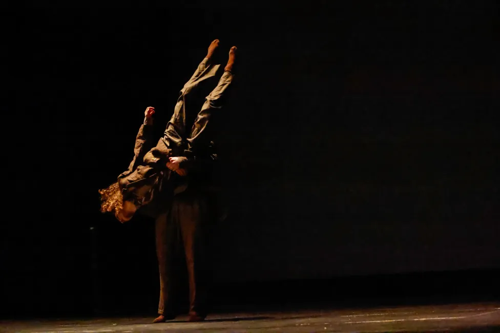 Two dancers dressed in black, starkly lit from the left only, one holder the other upside down.