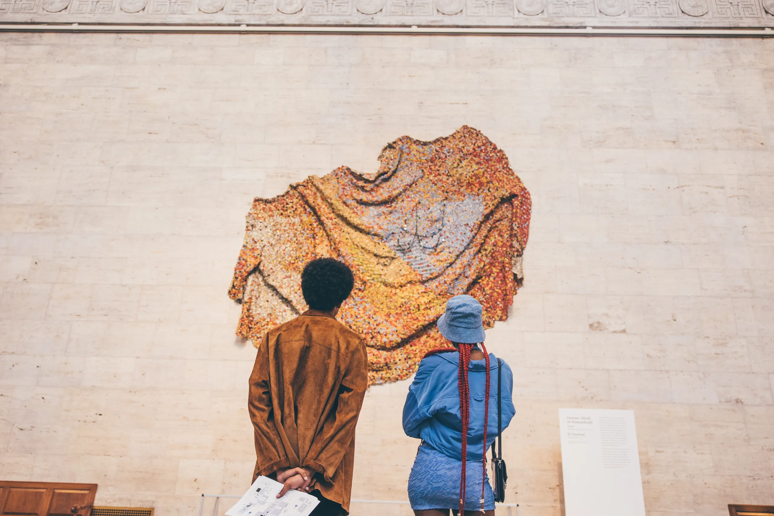 Two visitors stare at the large El Anatsui installation in the Great Hall of the DIA