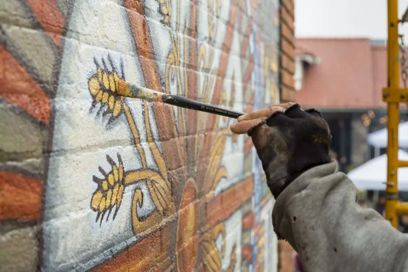 A DIA Partners in Public Art partner artist paints stalks of wheat onto a mural