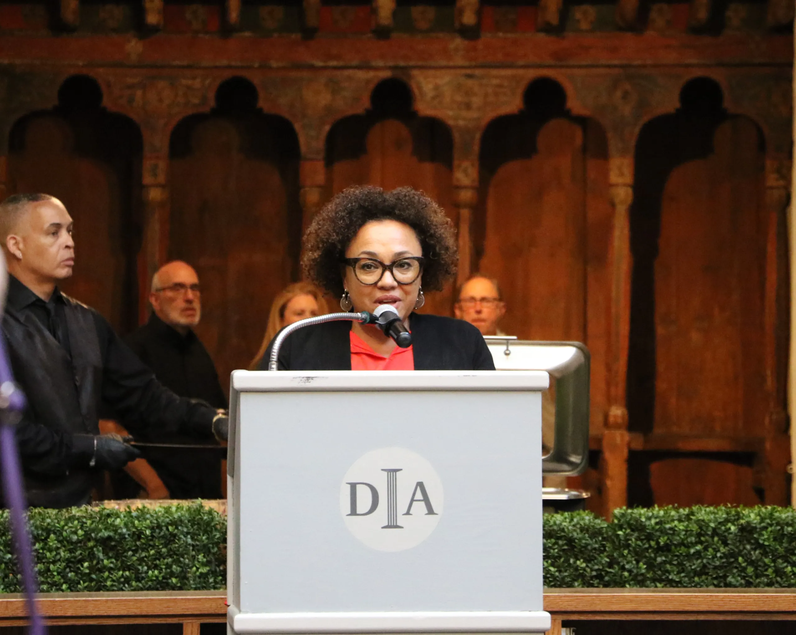 A Black woman with short, curly hair stands at a podium emblazoned with the Detroit Institute of Arts' logo.