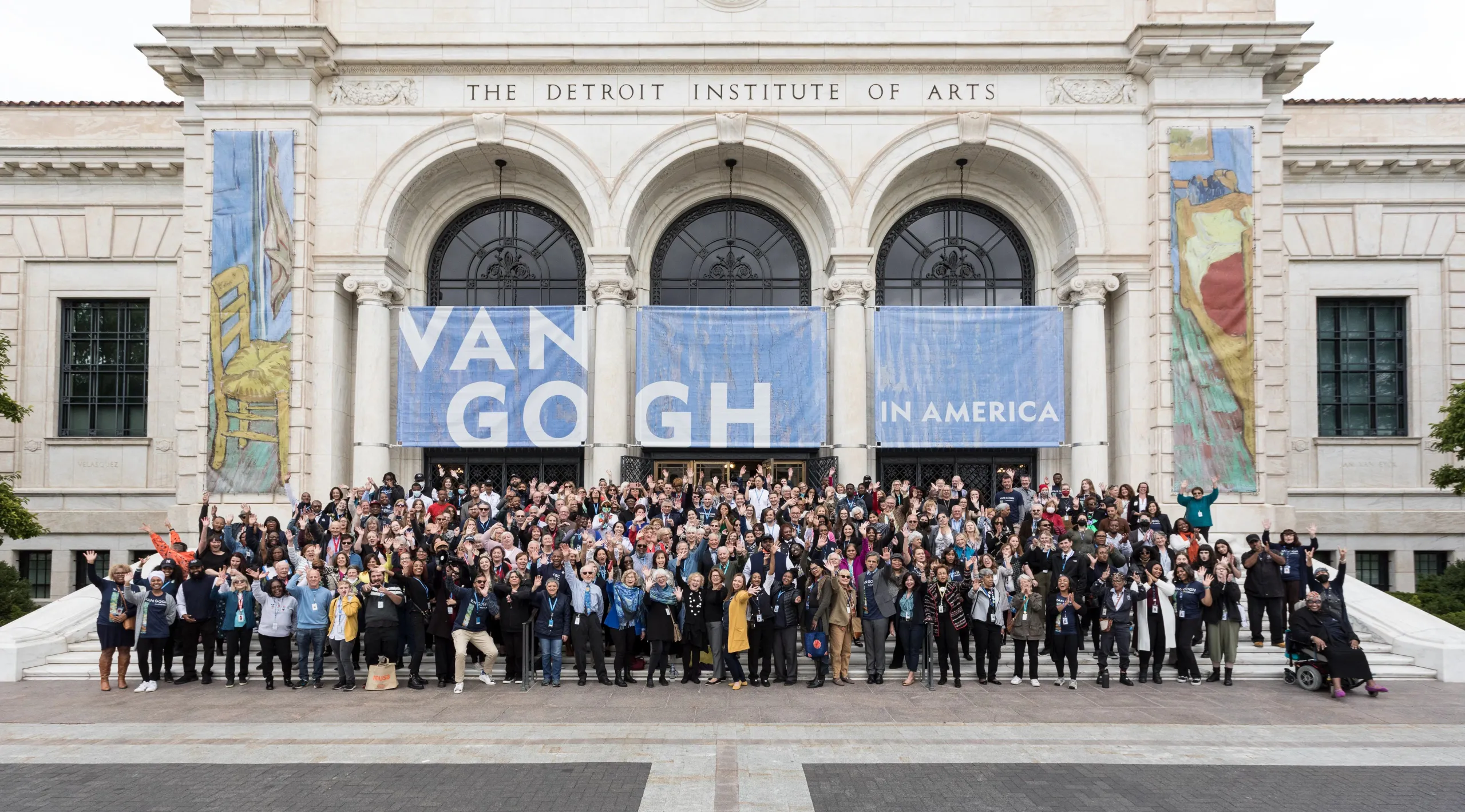 Detroit Institute of Arts staff pose together on the front steps of the museum under a banner that reads "Van Gogh in America."