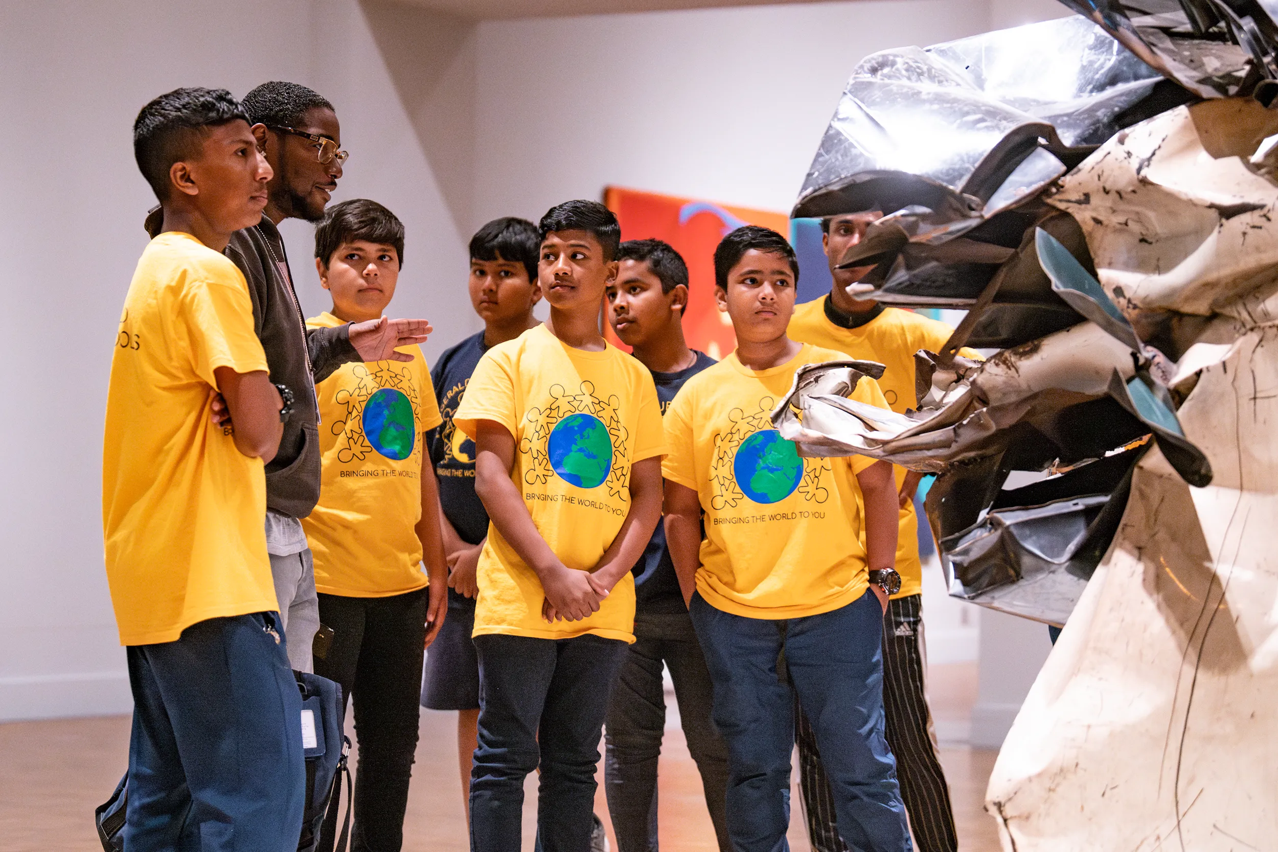 A group of students in yellow shirts listening to a DIA gallery teacher talk about a work of modern art. 