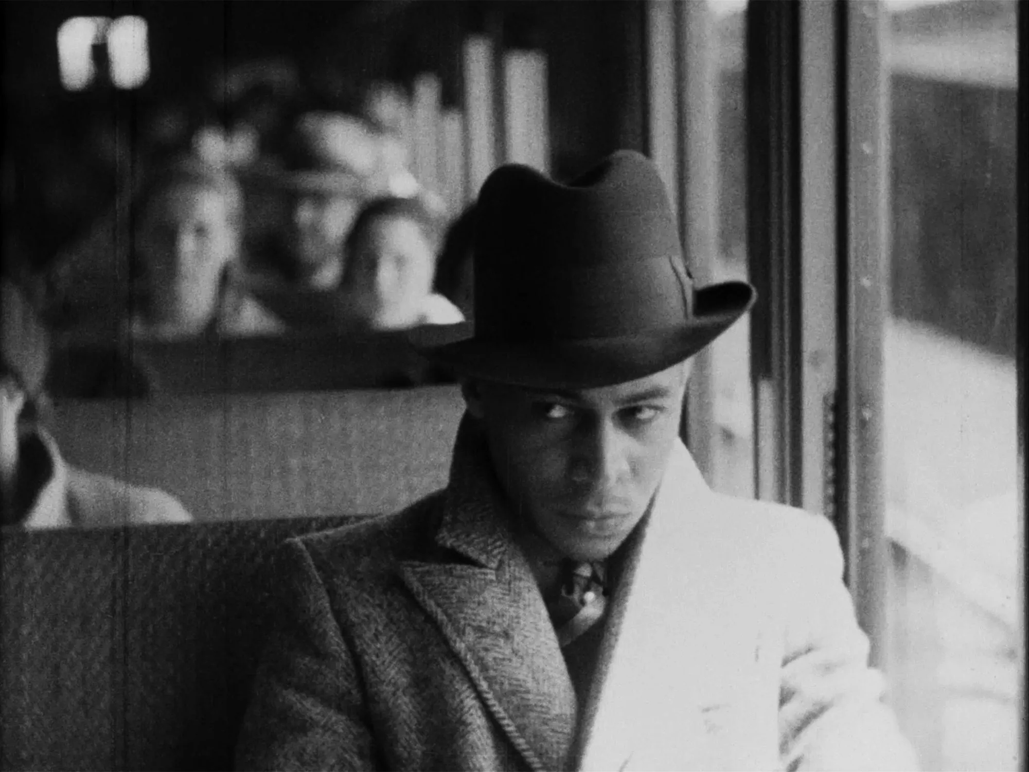 A man sitting on a bus in a coat, suit and hat