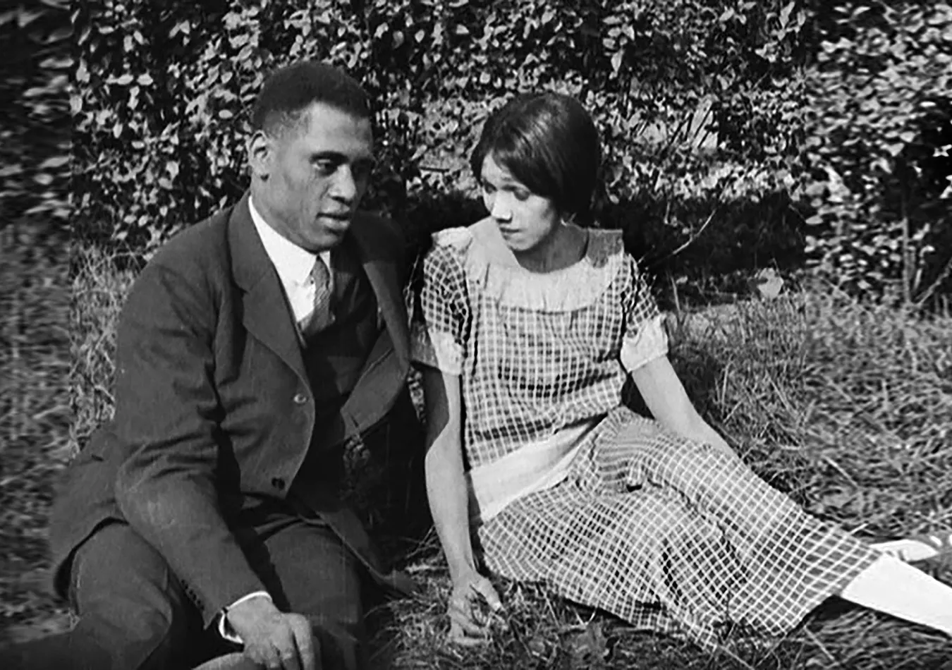 A man and a woman sit on the grass together in nice clothes.