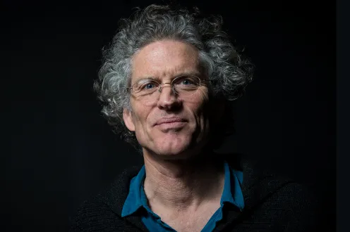 A headshot of poet David Hinton, wearing wire-rimmed glasses and a collared blue shirt, with curly gray hair.