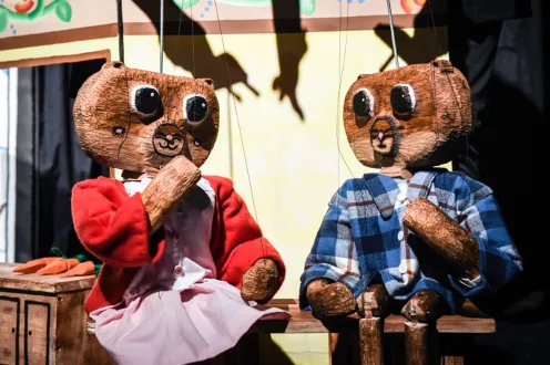 Two wooden puppet bears sat next to each other on a wooden bench as if in active conversation.
