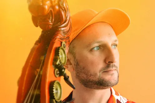 Florent Ghys pictured with his bass in a orange baseball cap in front of an orange background.