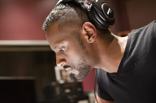 Carlos Simon pictured in a recording studio wearing large over-the-ear headphones.