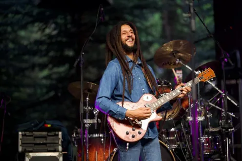 Julian Marley smiles as he performs on stage with a guitar.