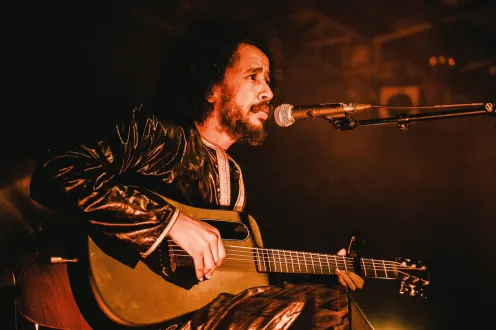 A man sits in front of a microphone and plays an acoustic guitar.