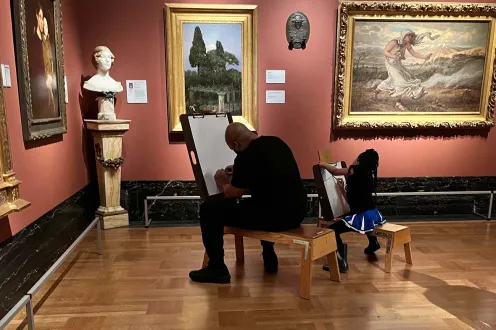 An adult and a young child sit together on separate easel stools