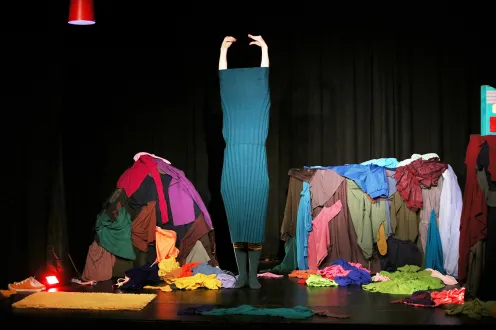 A stage full of colorful clothes and someone getting stuck getting dressed.