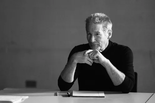 In this still from the film, Oh Canada, a man in a long-sleeved black shirt sits with his elbows resting on a table.