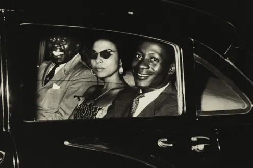 Two men and a woman sit in the backseat of a car