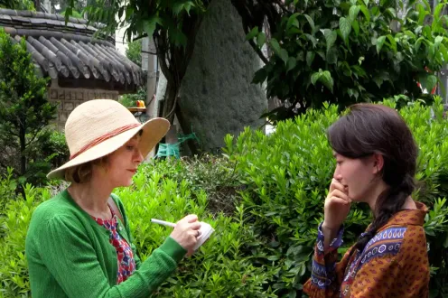 Two women stand facing each other in a garden