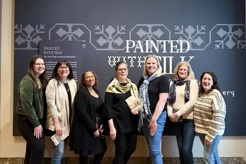 A group of seven people stand in front of the entrance to the exhibition "Painted with Silk"