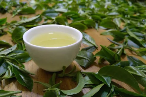 A white tea cup with green tea surrounded by leaves