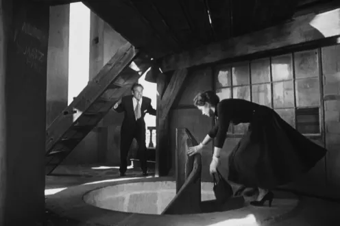 A woman starting down a spiral staircase with a man chasing behind