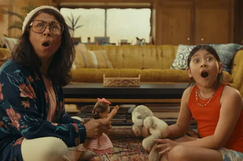 A mom and child sit on a living room floor in shock