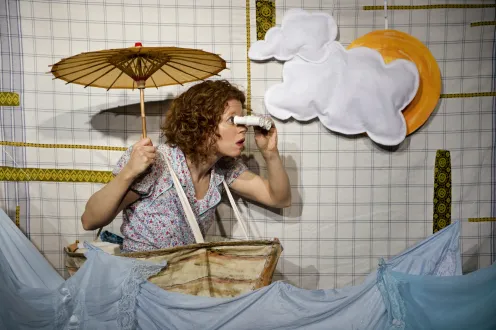 Whimsical woman with parasol using binoculars in a sea of fabric