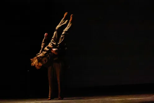 Two dancers dressed in black, starkly lit from the left only, one holder the other upside down.
