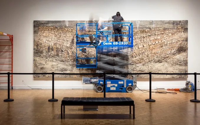 Conservators work on a larger than life painting with the use of a scaffold