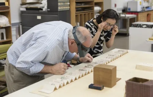 Paper conservators closely examining a work on unfolded paper 