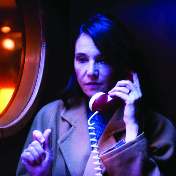 A woman in a brown coat talks on an older-style, corded phone.